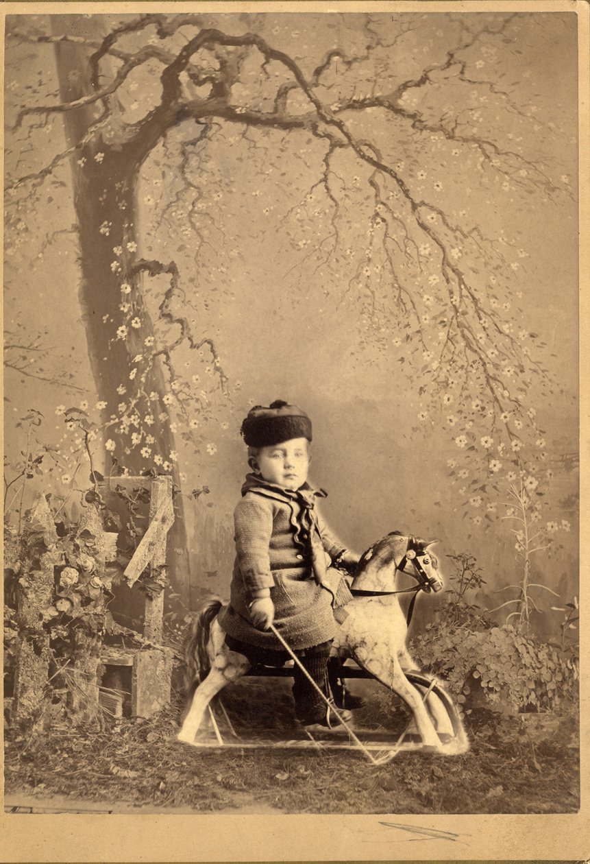 Ung pojke sittande på en gunghäst med stor målad bakgrund, 1880-tal (albumintryck) av American Photographer