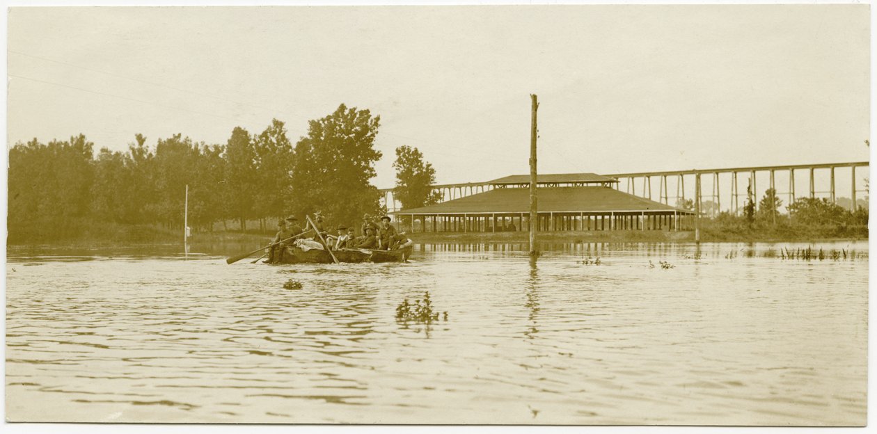 Horizontal, sepia photograph showing uniformed soldiers paddling a rowboat across a large flooded area av Carl Michel