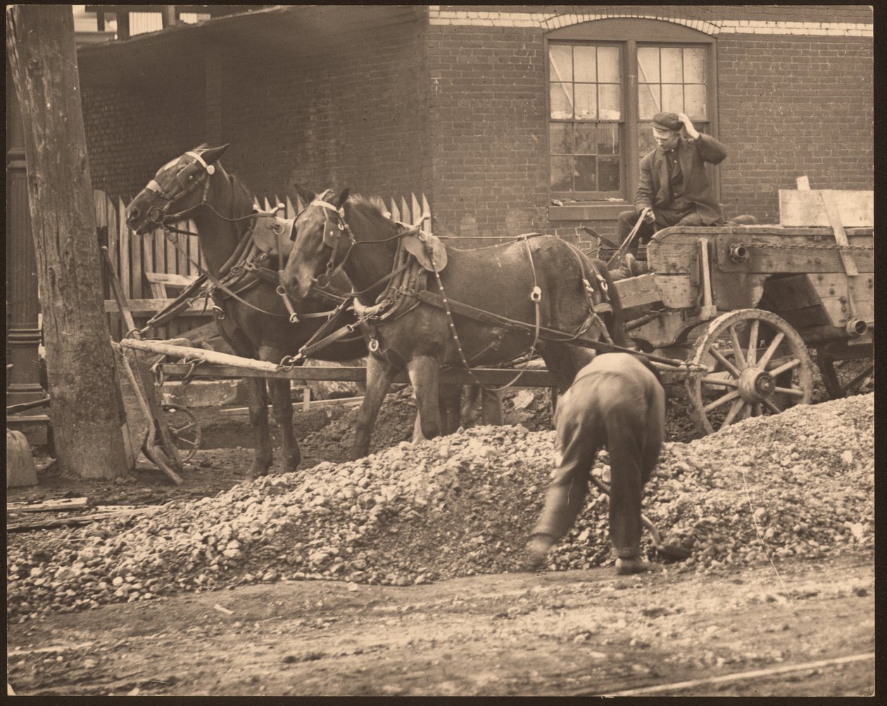 Horizontal, black and white photograph of a horse-drawn wagon at a construction site. A man shovels dirt and rock while another drives the wagon av William G. Swekosky